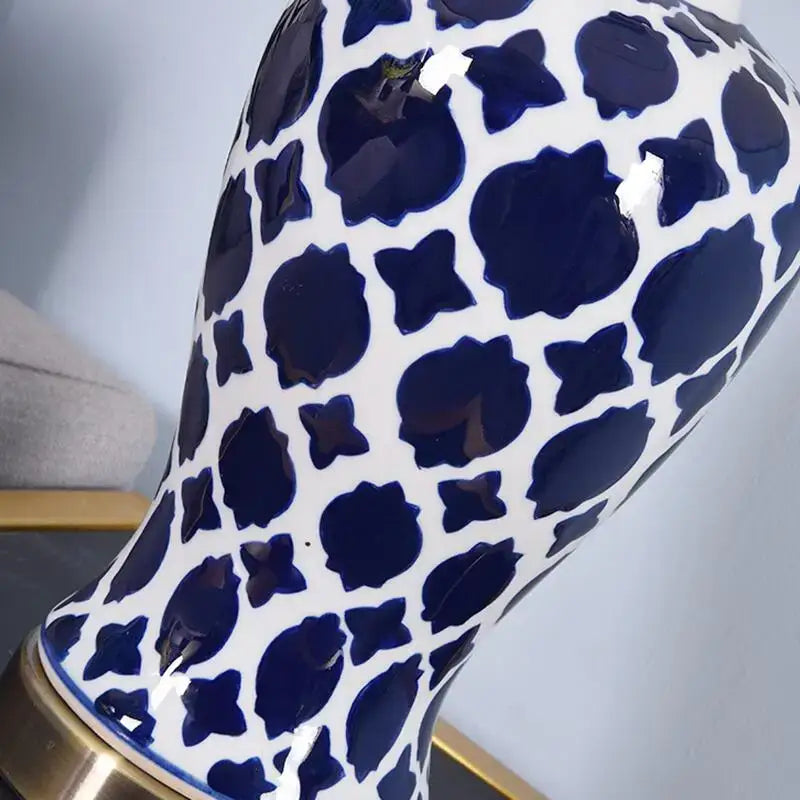Glossy white ceramic vase with bold blue leopard print near a geometric blue ceramic bedside table lamp with gold base