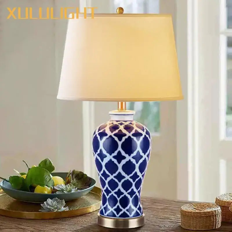 Blue ceramic bedside table lamp with white geometric pattern, gold-toned base, and cream fabric shade for bedroom