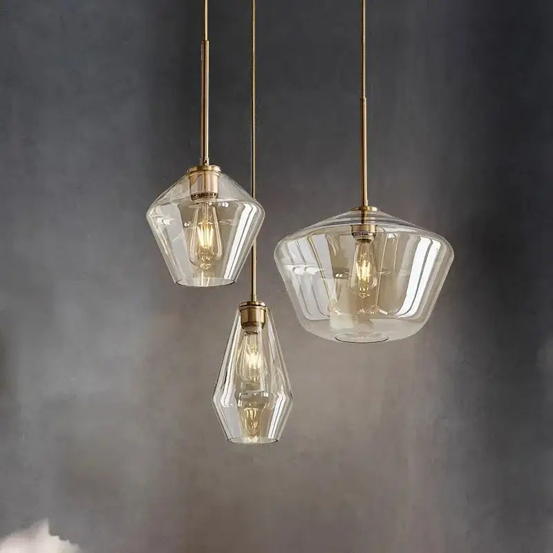 Three geometric glass chandelier pendant lights with brass accents and exposed filament bulbs for kitchen lighting