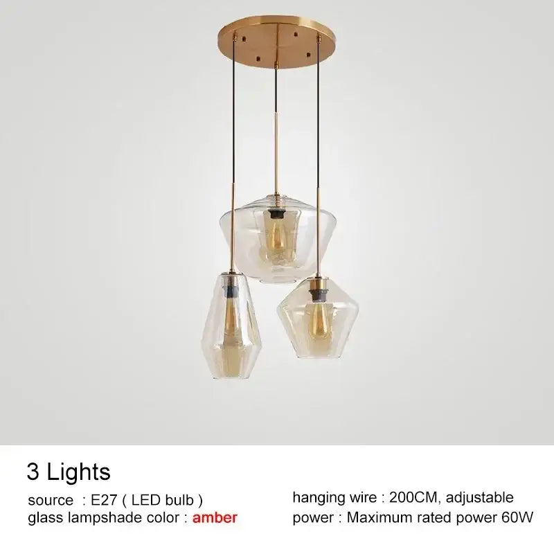 Modern brass-finished pendant light with three clear amber glass lampshades in varying geometric shapes for kitchen lighting