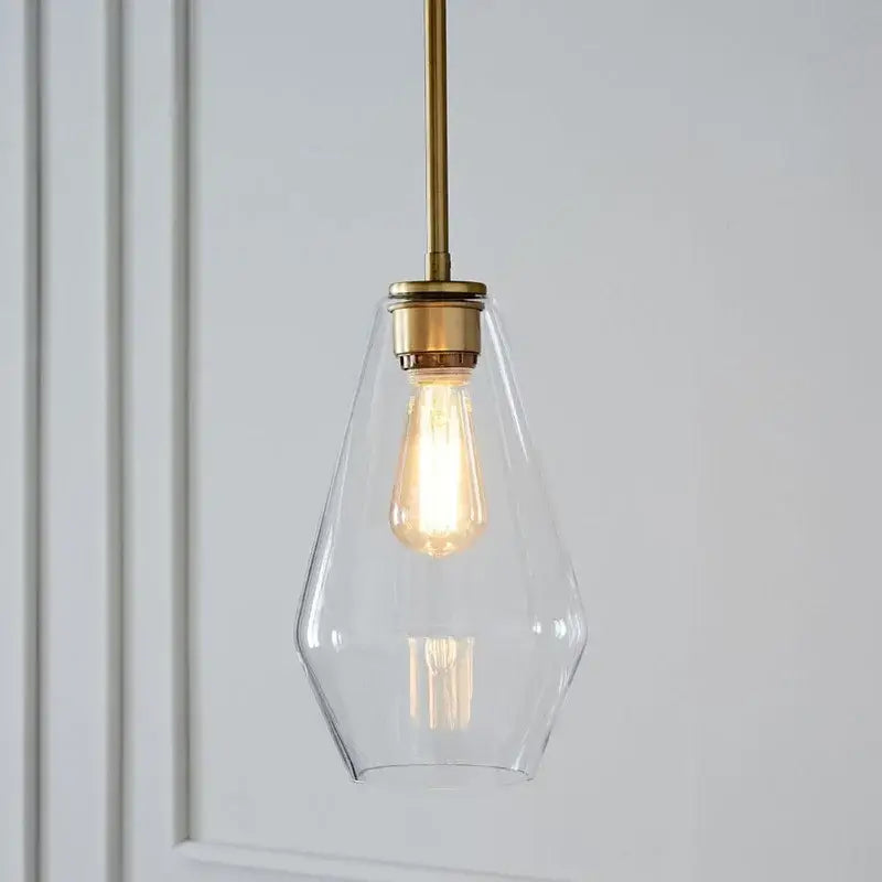 A clear glass pendant light with brass-finished rod and exposed edison bulb in geometric glass pendant lights set