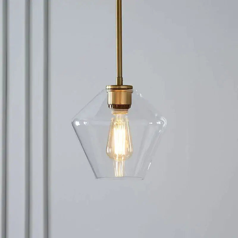 A clear glass pendant light with brass finish and exposed filament bulb from a geometric pendant lights set for living room