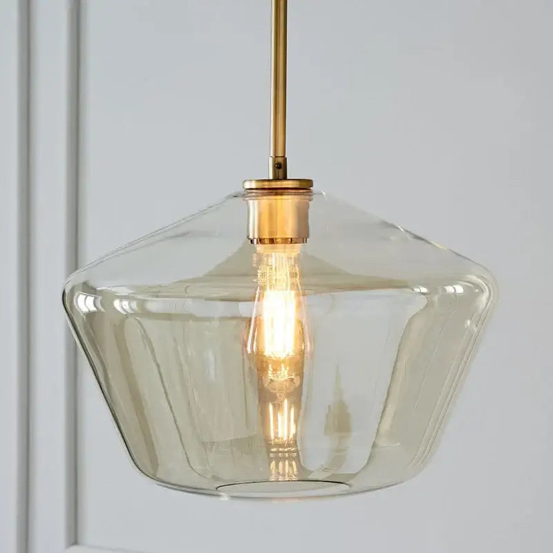 A modern pendant light with a clear faceted glass shade and brass hardware in a geometric pendant lights set for living room