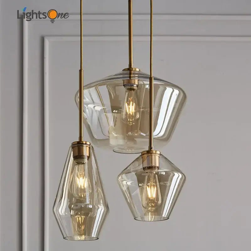 Set of three brass glass pendant lights with clear geometric shades and exposed filament bulbs for living room use