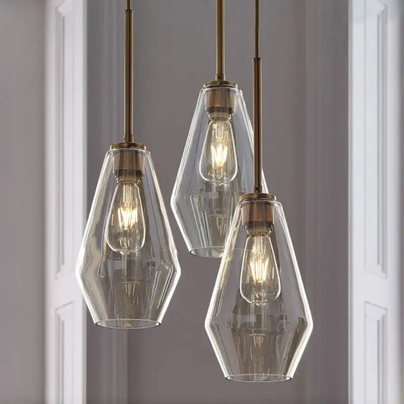 Three clear glass pendant lights with brass accents and exposed filament bulbs in a geometric pendant lights set