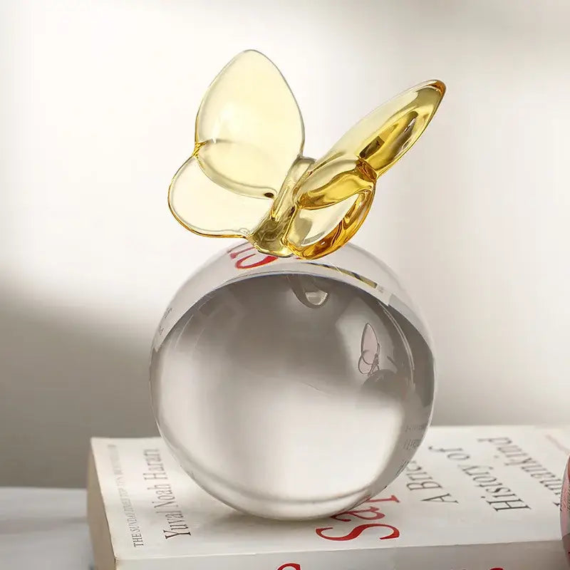 A translucent amber glass geometric butterfly perched atop a clear crystal ball for home decor use