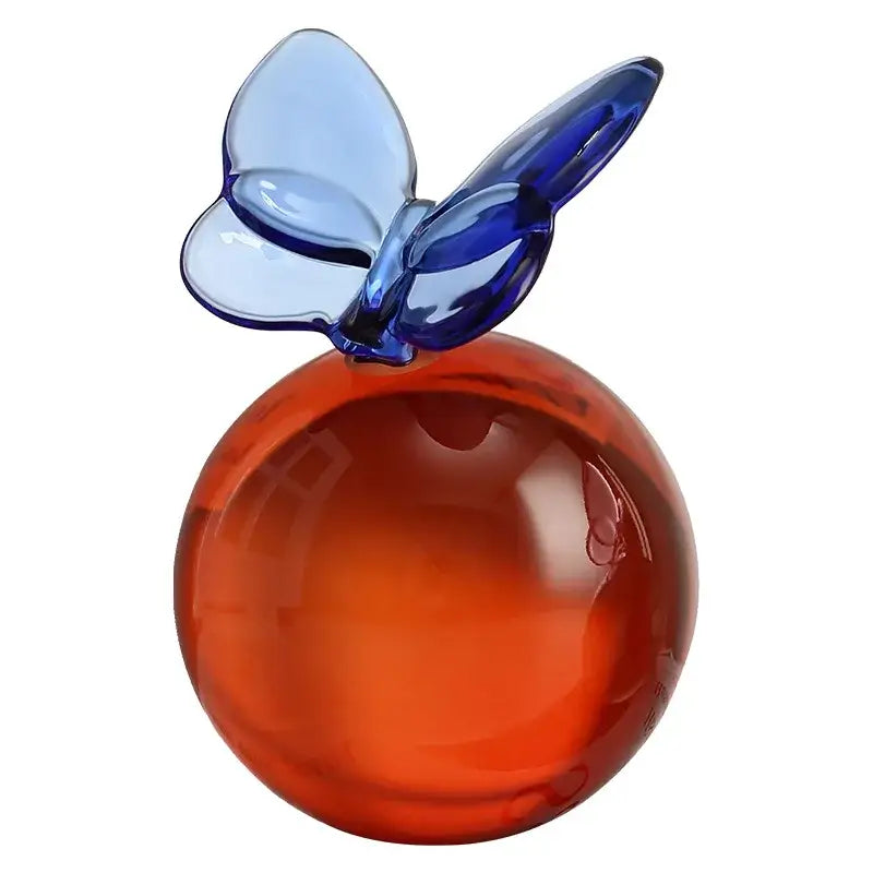 A translucent orange glass apple ornament with a blue geometric butterfly on top for crystal ball home decor