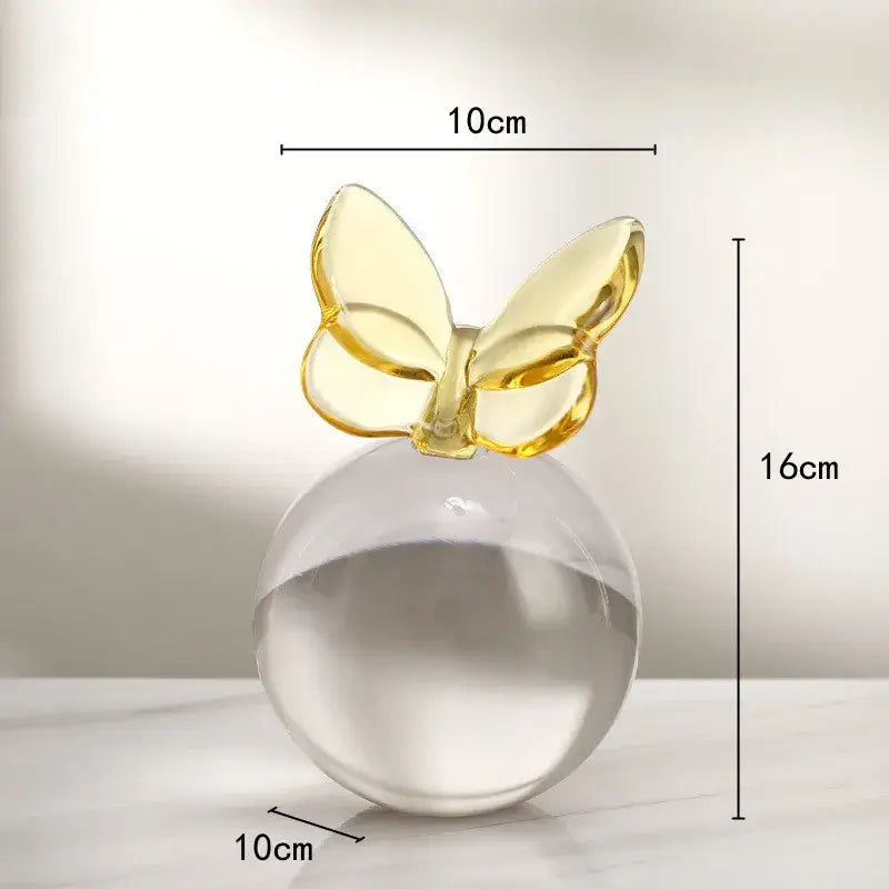 Transparent glass crystal ball with a gold geometric butterfly on top in blue and pink home decor style
