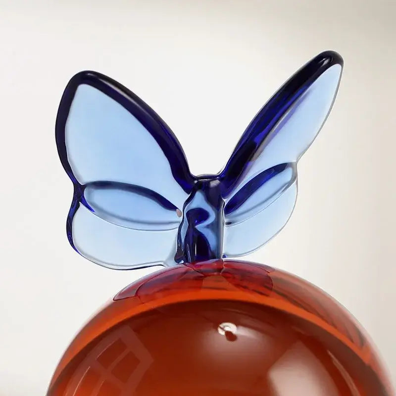 A geometric butterfly in translucent blue glass perched on a glossy amber crystal ball for home decor