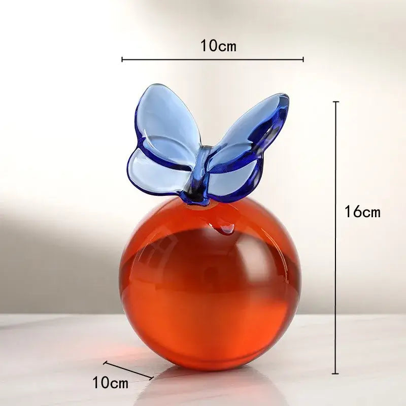 A translucent orange glass apple ornament with a delicate blue geometric butterfly crystal ball for home decor