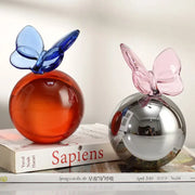 Two translucent glass crystal ball sculptures with blue and pink geometric butterfly accents for home decor