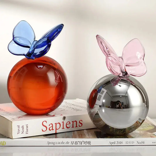 Two translucent glass crystal ball sculptures with blue and pink geometric butterfly accents for home decor
