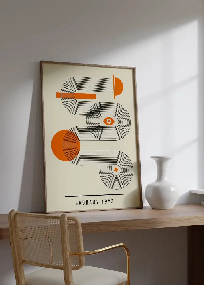 A framed bauhaus geometric canvas print in orange black on cream with a light wood frame for home decor