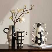 A white ceramic vase with black geometric check pattern and sculpted wavy handles for living room decor