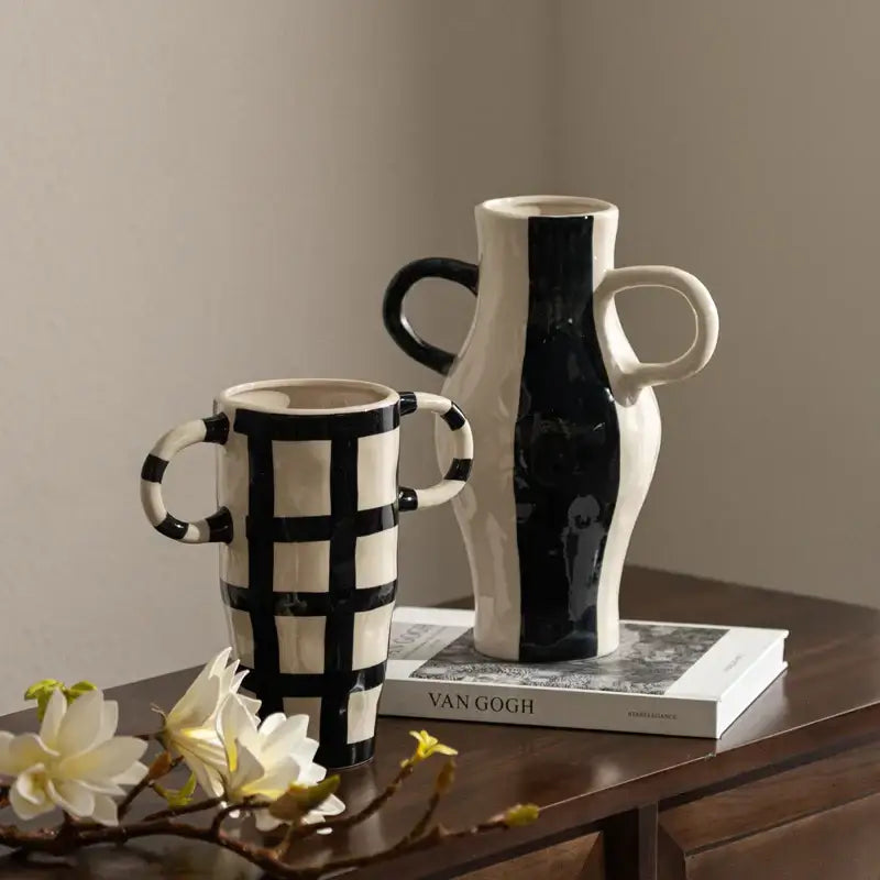 Cream-colored ceramic vase with bold black vertical stripe and sculpted handles featuring geometric check pattern decor