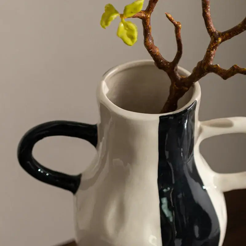 A ceramic vase with a geometric check pattern in white and black featuring two handles and a branch with green leaves