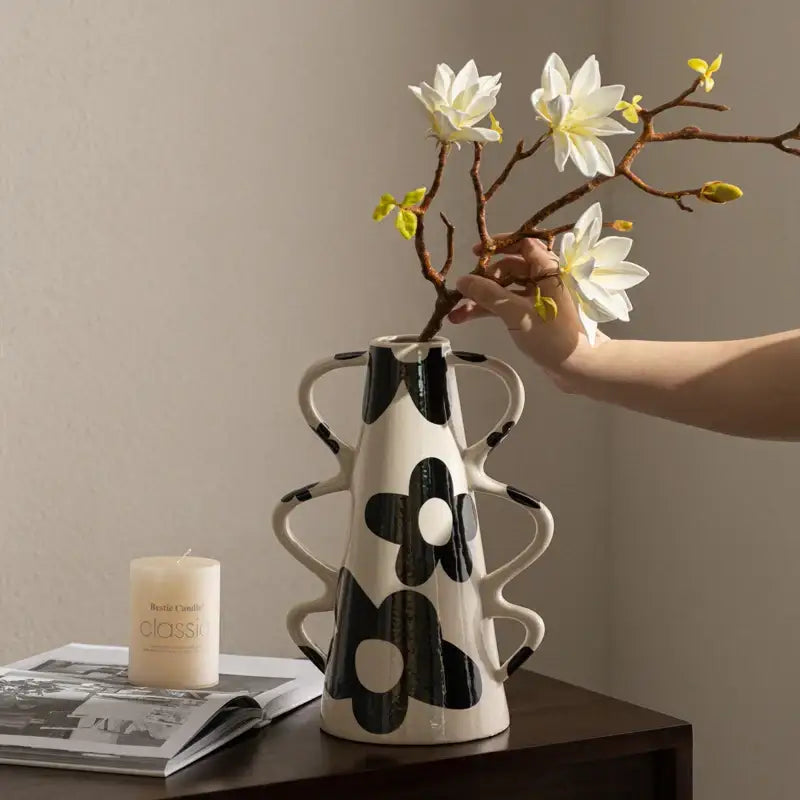 White ceramic vase with bold black floral and geometric check pattern featuring sculpted handles for living room decor