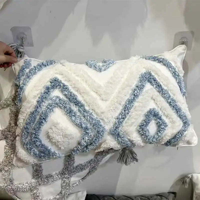 A geometric diamond tufted blue and white pillow with textured yarn embroidery and gray tassels for living room decor