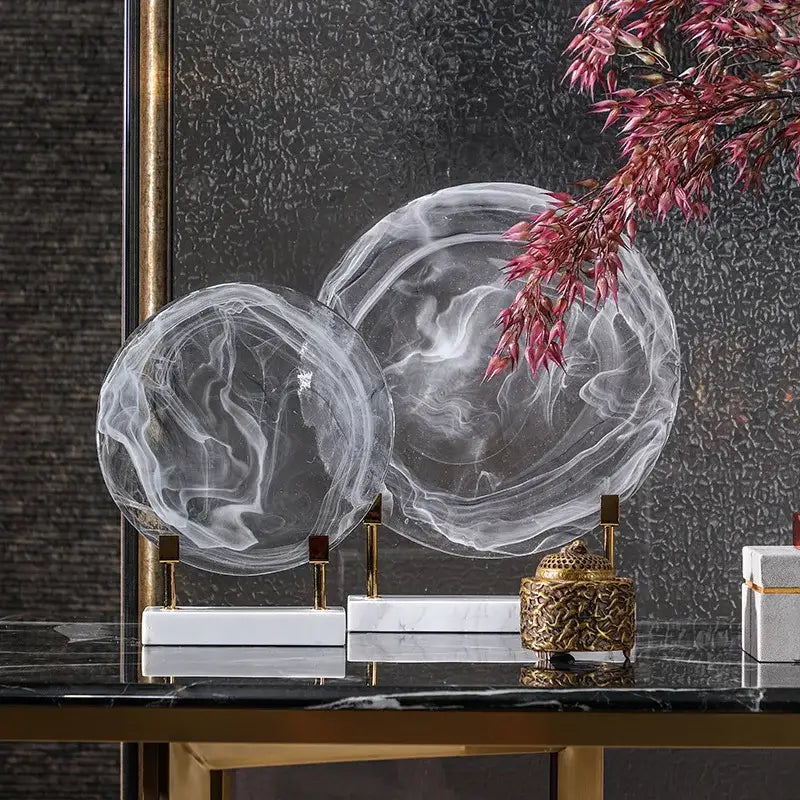 Two translucent swirling disk marble clear glass orbs on gold stands with white marble bases for home decor