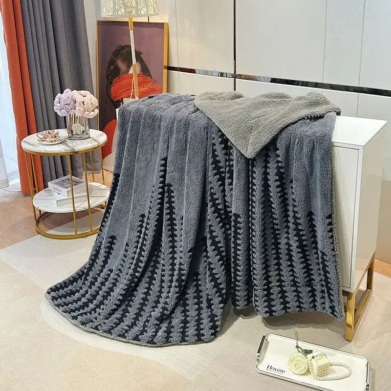 A plush gray geometric double layer lamb fleece blanket draped over a white cabinet for bedroom use