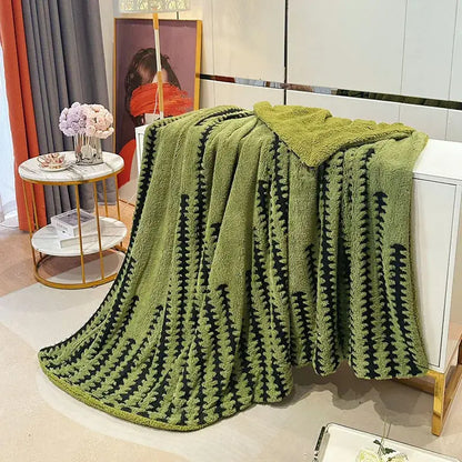 A plush olive green geometric double layer lamb fleece blanket with a textured black pattern draped over a white cabinet