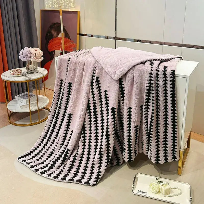 A plush pink and black geometric double layer lamb fleece blanket draped over a white cabinet for bedroom use