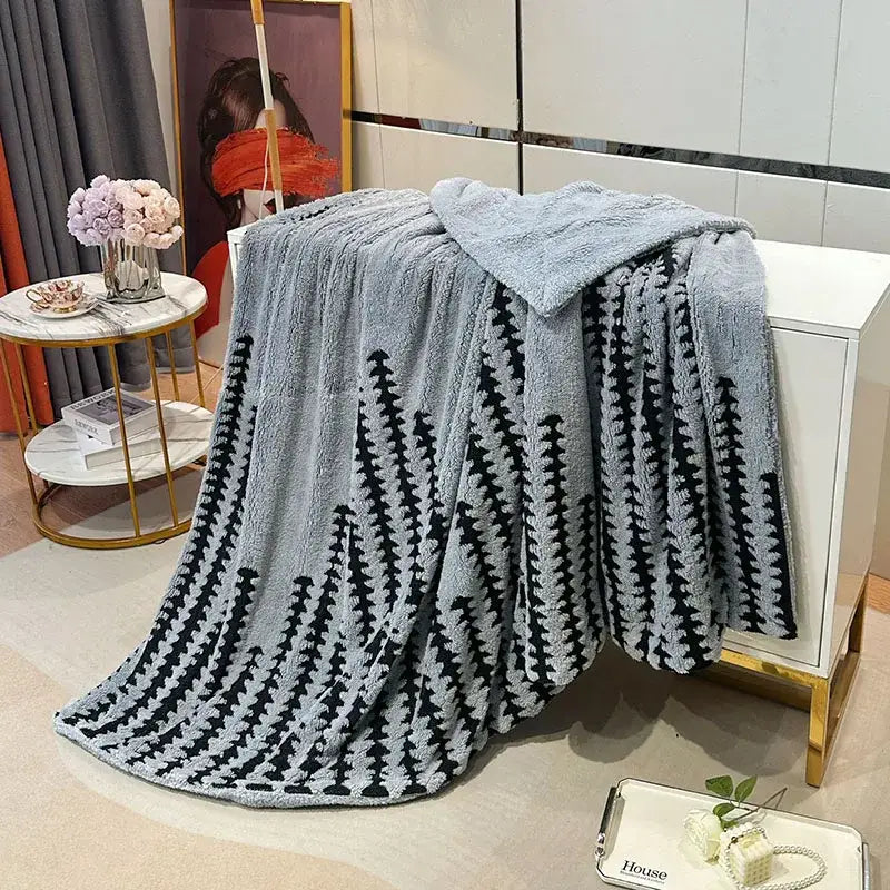 A soft light gray geometric double layer lamb fleece blanket with a black tree pattern draped over a white cabinet