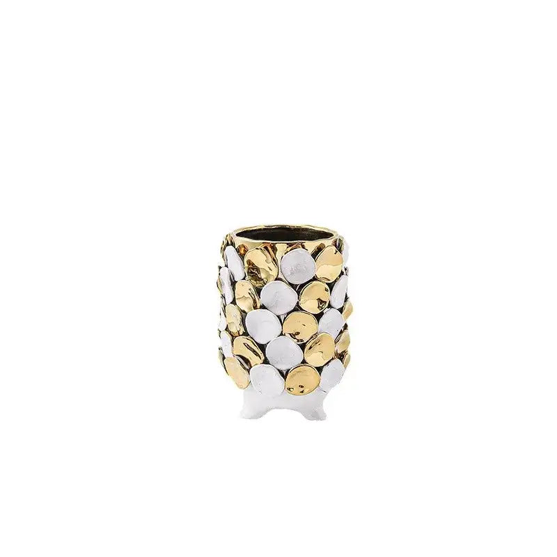 A cylindrical ceramic vase with geometric gold leaf relief featuring white and gold discs and three small feet for decor