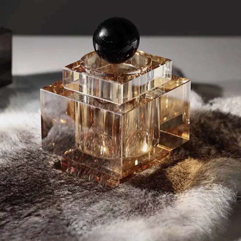 A sleek geometric storage jar with faceted amber glass and black spherical stopper for bedroom jewelry storage