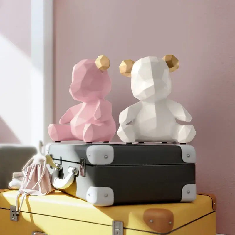 Two geometric bear figurines resin sculpture in pink and white with gold-tipped ears on vintage suitcase decor