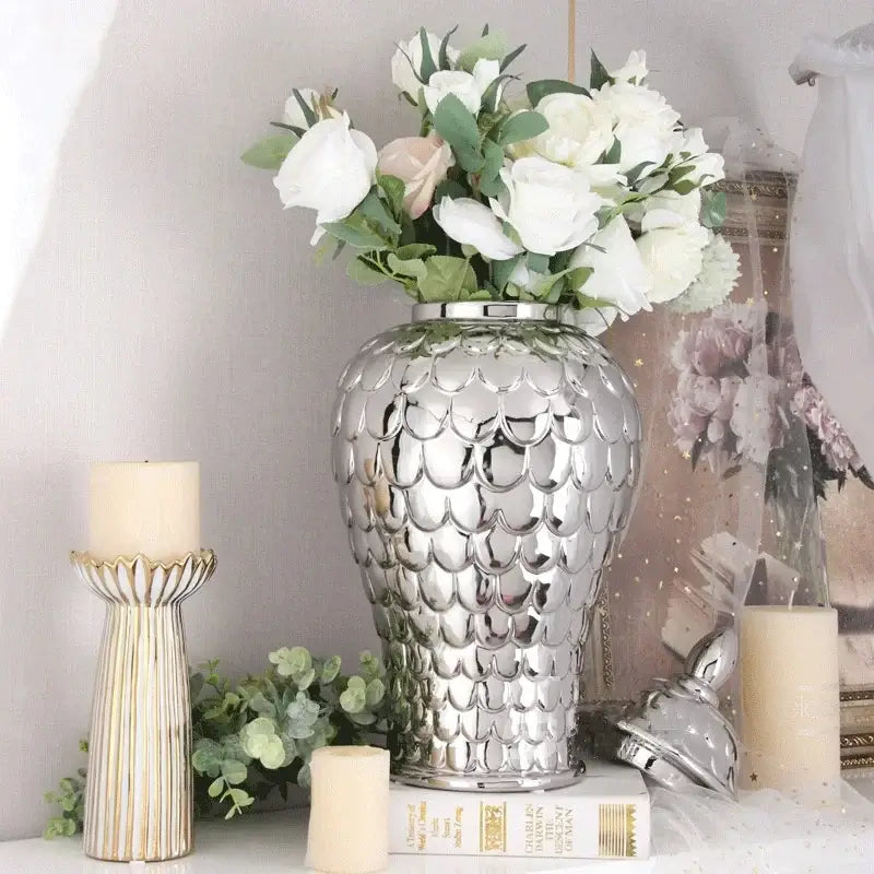 Shiny silver porcelain jar with scalloped fish-scale pattern holding white roses in decorbites geometric golden style