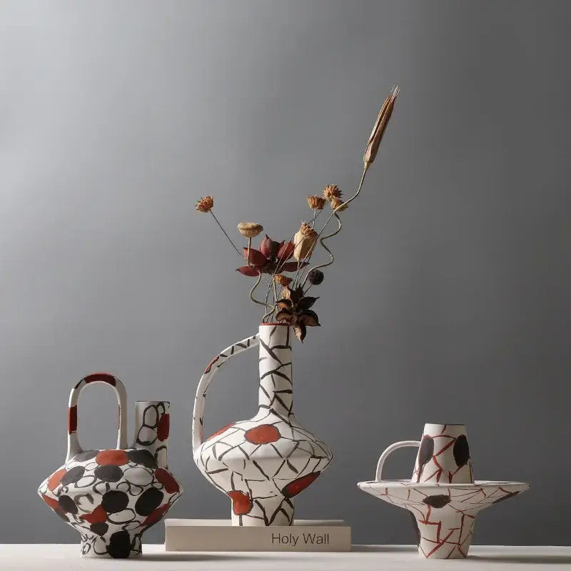 White ceramic geometric graffiti ceramic vase with black terracotta patterns and curved handle holding dried flowers