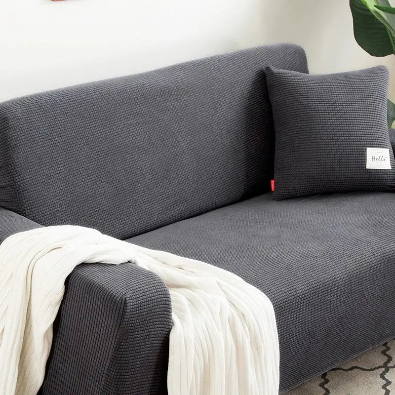 Dark gray geometric textured stretch sofa cover with waffle pattern pillow and cream throw blanket for living room