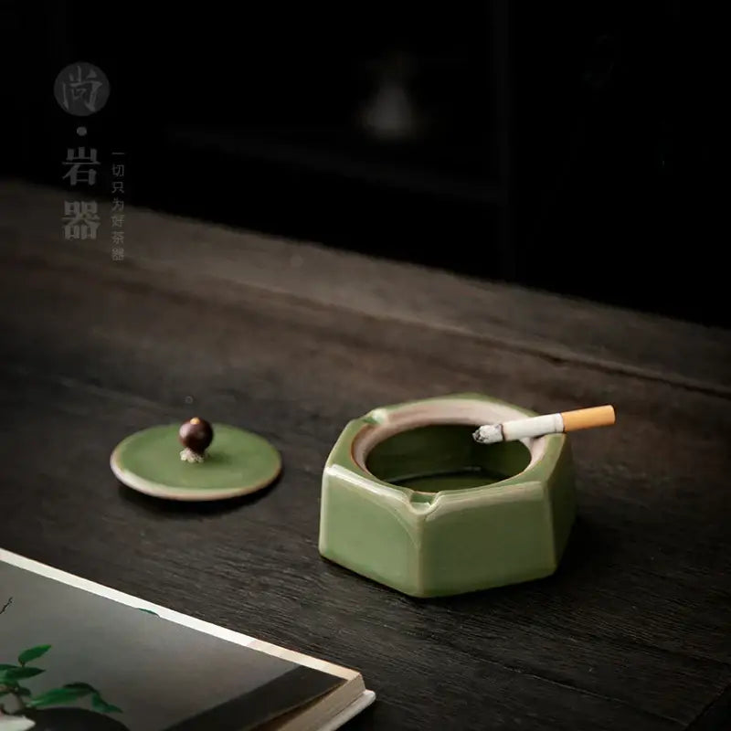 Green ceramic ashtray with geometric hexagonal design and lid featuring dark knob and cigarette for office desk decorbites geometric green