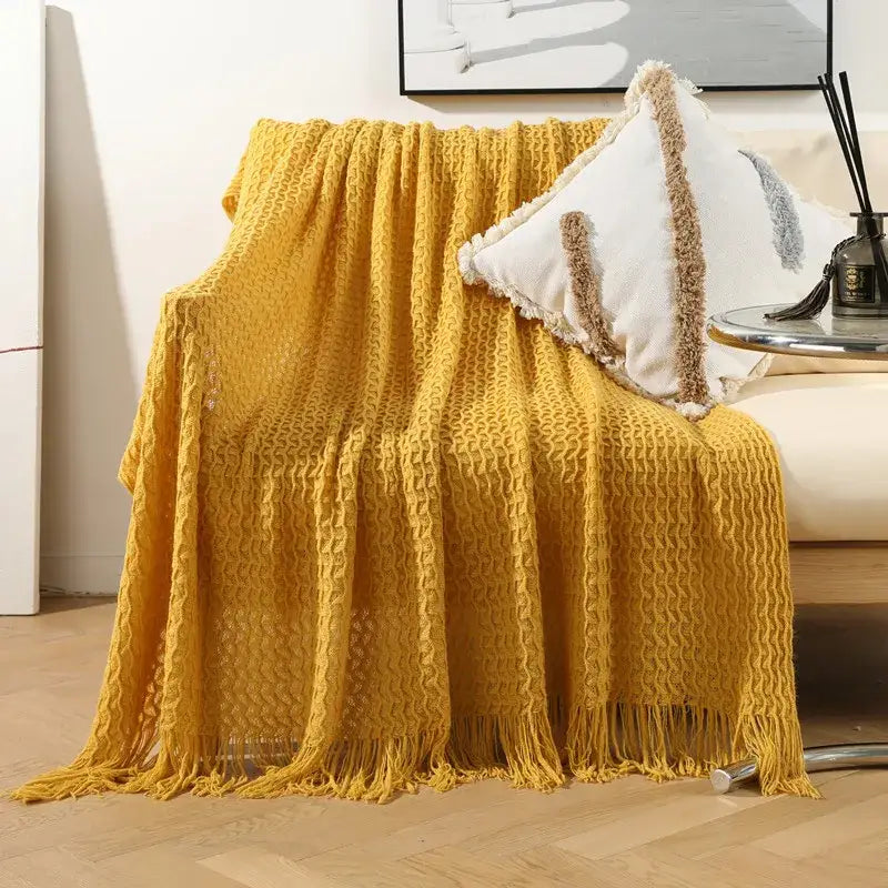 A cozy mustard-yellow decorbites geometric knit sofa blanket with waffle texture and tassel fringe for living room decor