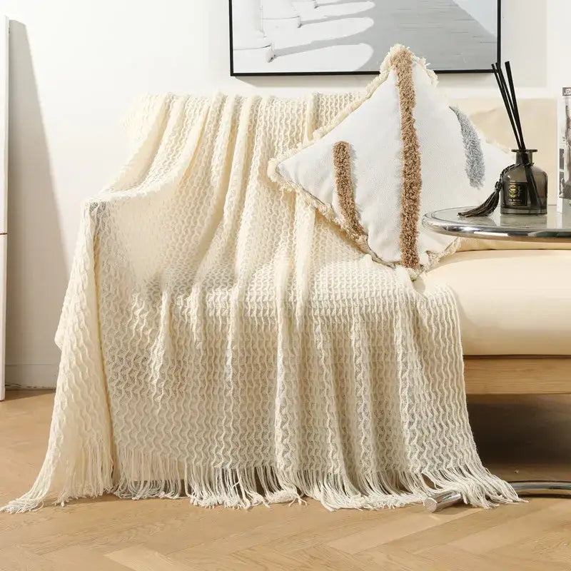 Cream-colored geometric knit sofa blanket with textured tassel fringe for living room decor by decorbites