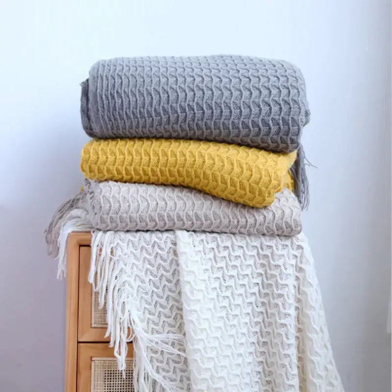 Stack of four decorbites geometric knit sofa blankets in gray yellow beige and white with fringe tassel detailing