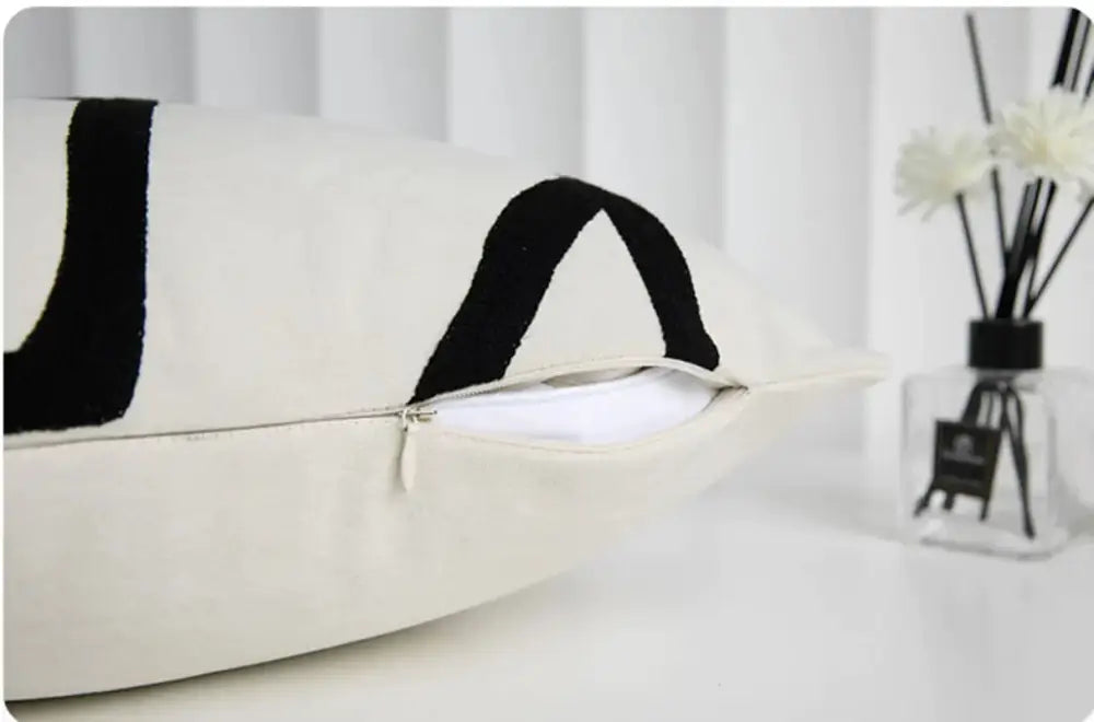 Cream-colored geometric line embroidered pillowcase with bold black abstract patterns and visible zipper closure for decorbites