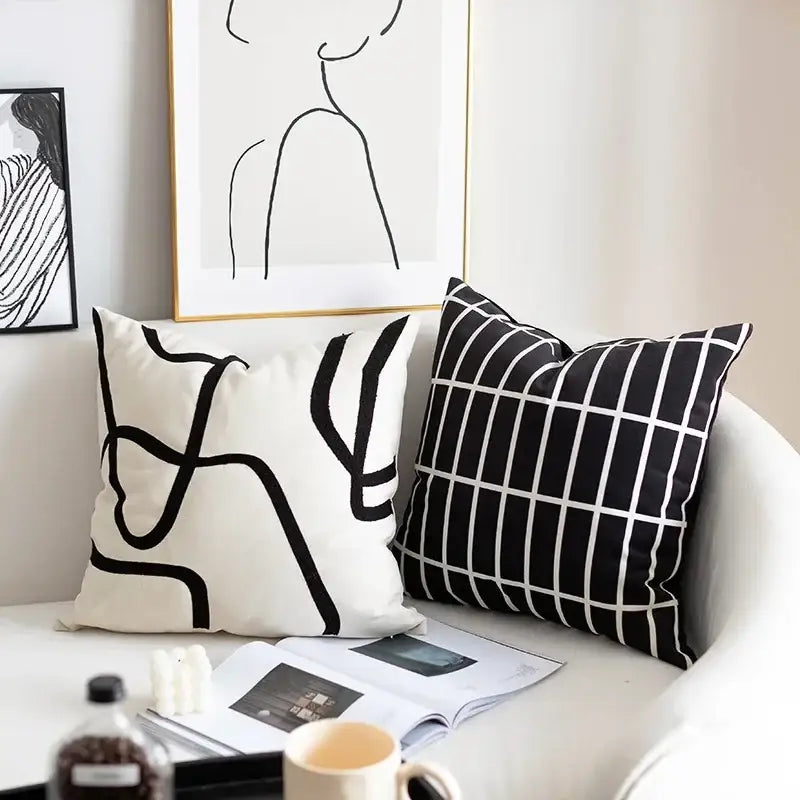 Two black and white geometric line embroidered suede throw pillows with abstract patterns on white curved sofa for decorbites decor