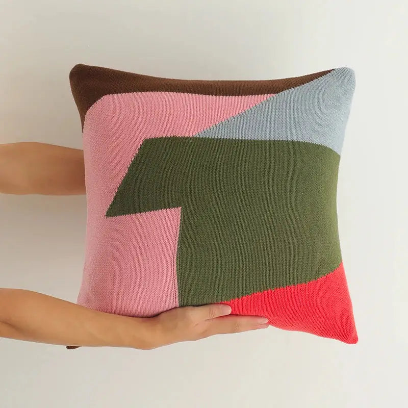 A square knitted cushion cover featuring a modern geometric pattern in pink olive green light blue and coral red for living room decor