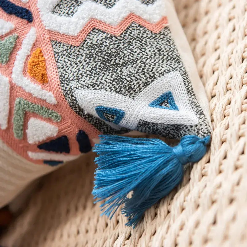 Colorful geometric embroidered cushion cover in pink white blue and green with turquoise tassel on gray fabric base