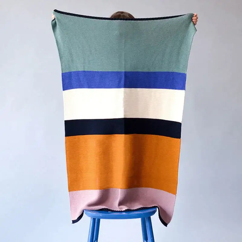 A cozy decorbites knitted chenille blanket with ribbed knit and bold horizontal stripes in teal, navy, and mustard yellow