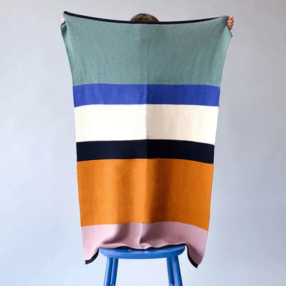 A cozy decorbites knitted chenille blanket with ribbed knit and bold horizontal stripes in teal, navy, and mustard yellow