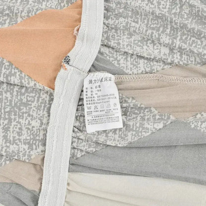Gray and beige patterned elastic bedsheet with white care label on the back side of an elastic armless futon sofa cover