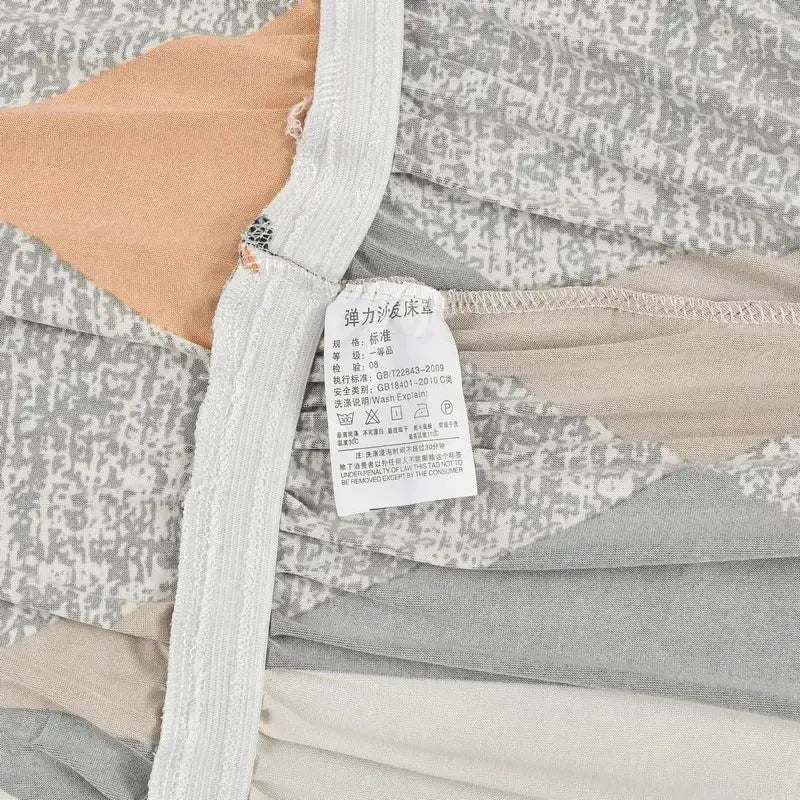 Gray and beige patterned elastic bedsheet with white care label on the back side of an elastic armless futon sofa cover
