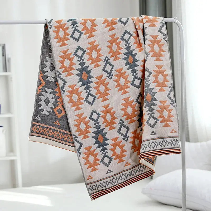 A cream-colored decorbites cotton gauze bath towel with orange and gray geometric pattern for bathroom use