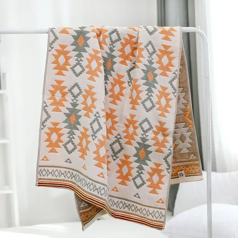 A cream-colored decorbites cotton gauze bath towel with bold orange and gray geometric tribal-inspired patterns and layered borders
