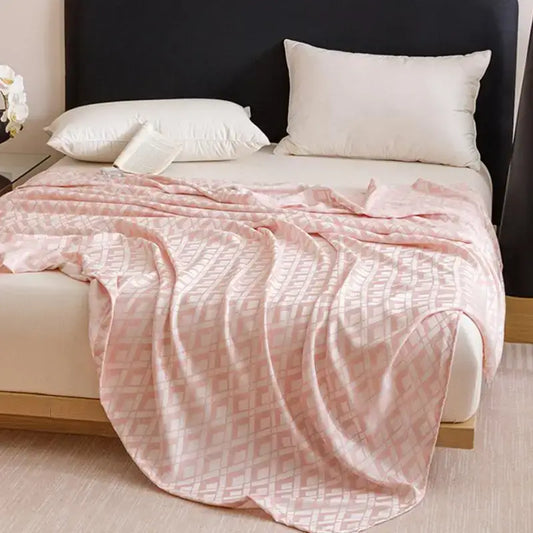 A soft pink bamboo fiber summer blanket with subtle geometric pattern draped over a bed for lightweight decorbites bedding