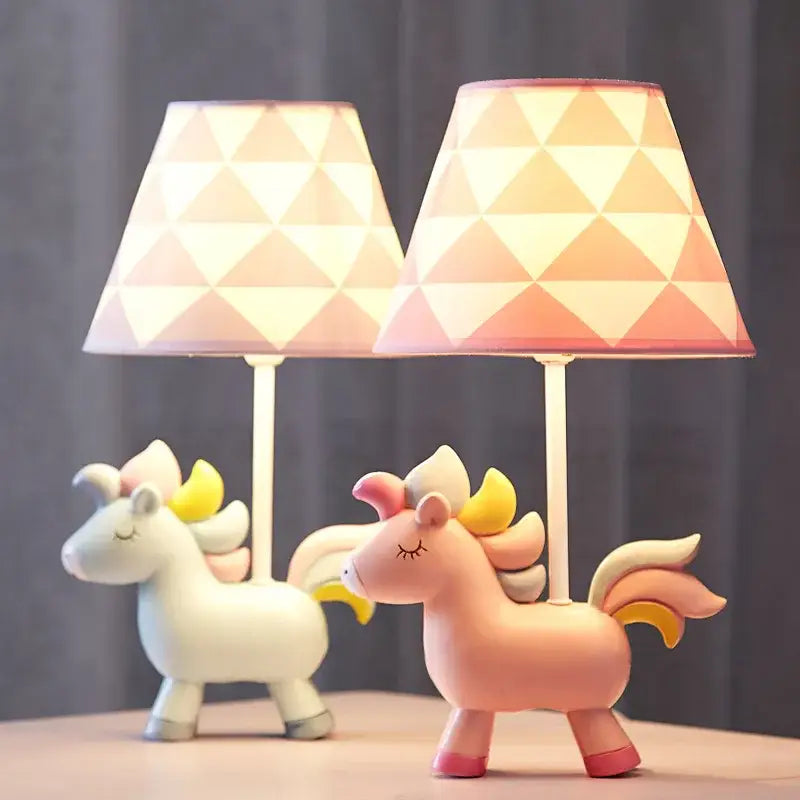 Two whimsical unicorn table lamps in white and pink with geometric patterned lampshades for children’s bedroom