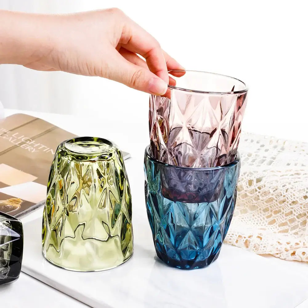 A stack of three colorful geometric pink faceted 240ml water glass drinkware tumblers with a hand lifting the top one